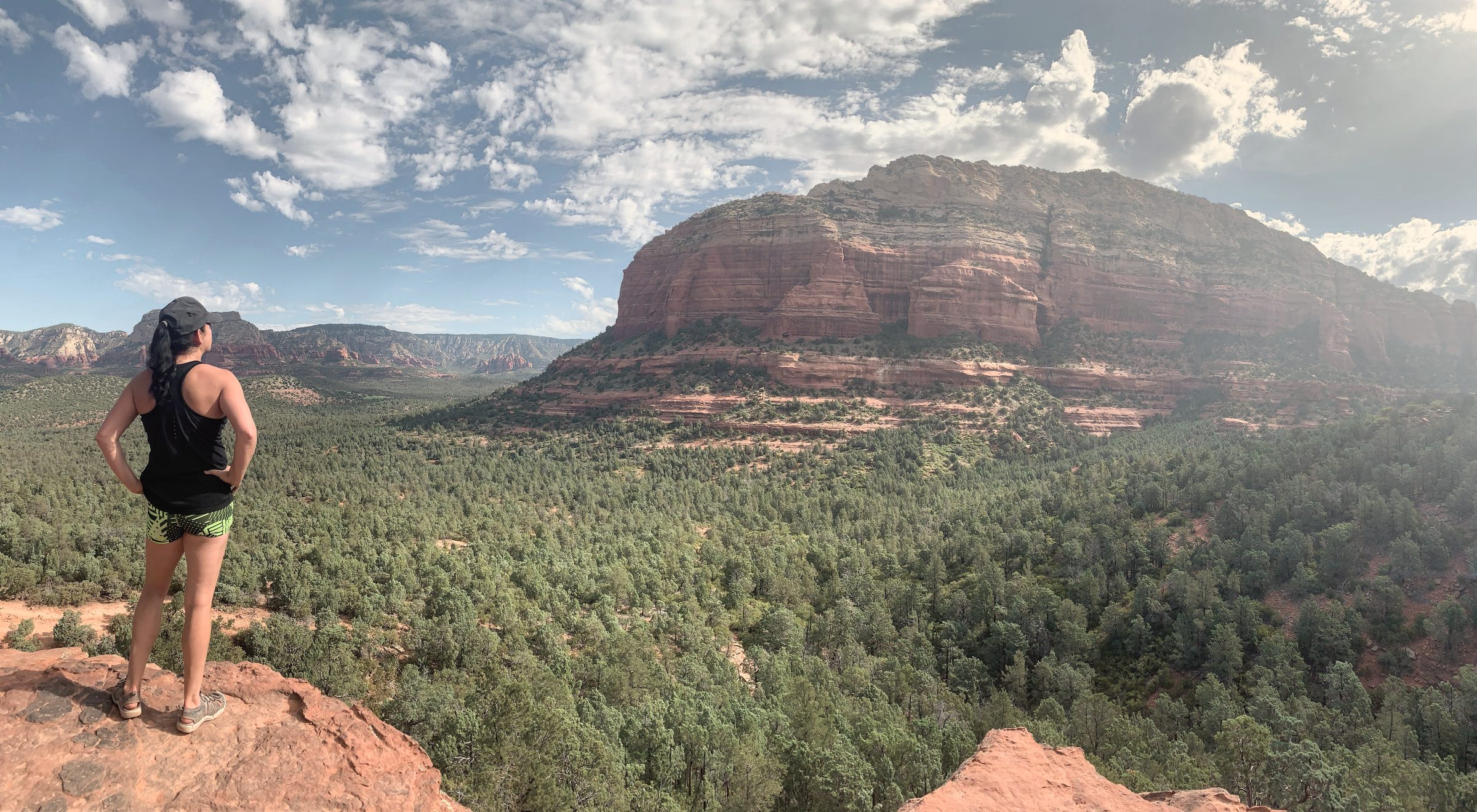 Lisa standing on red rock, looking out over a wide canyon and forest near Sedona